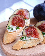 Close view of two sandwiches with goat cheese, fig and thyme on fresh crispy bread served on a wooden plate on light grey back