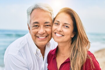 Obraz premium Middle age hispanic couple smiling happy and hugging walking at the beach