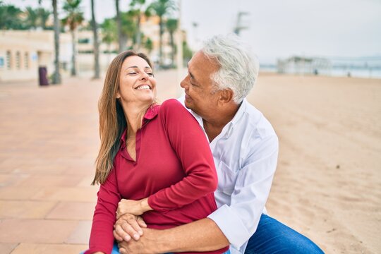 Middle age hispanic couple smiling happy and hugging sitting on the bench.