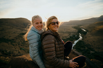 Caucasian mother and daughter bonding while watching beautiful sunset on top of luscious mountain