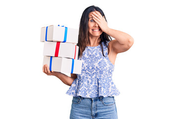 Young beautiful brunette woman holding birthday gift stressed and frustrated with hand on head, surprised and angry face