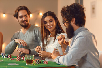 Happy young people playing poker sitting at table with drinks at casino themed party