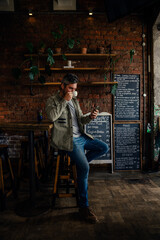Fototapeta premium Male customer sitting in authentic cafe sipping hot coffee chatting to mates on smartphone