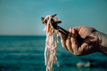 Woman holding pure white rice noodle with chopsticks at the beach, near the sea. Selective focus.