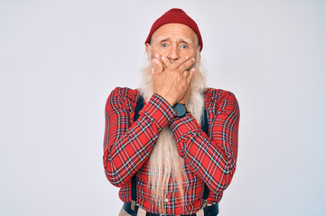 Old senior man with grey hair and long beard wearing hipster look with wool cap shocked covering...