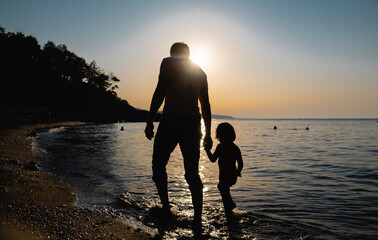 Father and son walking on the beach, stepping on waves at the sunset time. 