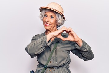 Senior grey-haired woman wearing explorer hat smiling in love showing heart symbol and shape with hands. romantic concept.