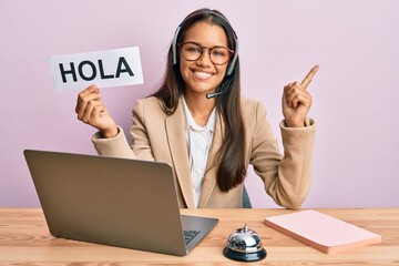 Beautiful hispanic woman wearing operator headset holding hola greenting smiling happy pointing with hand and finger to the side © Krakenimages.com