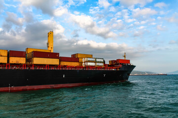 A stern part of the large sea cargo ship (container ship) leaving from the port close-up. Cloudy weather. Shallow focus.