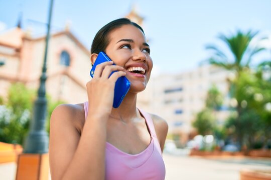 Young beautiful hispanic sporty woman wearing fitness outfit smiling happy and natural calling using smartphone at the town