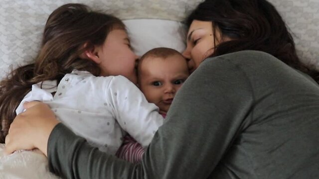 Mother and Older Daughter Smothering their Baby/Sister While Cuddling in Bed