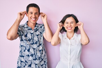 Beautiful couple wearing casual clothes smiling pulling ears with fingers, funny gesture. audition...