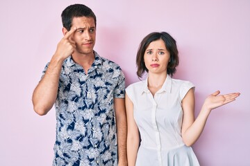 Beautiful couple wearing casual clothes confused and annoyed with open palm showing copy space and pointing finger to forehead. think about it.