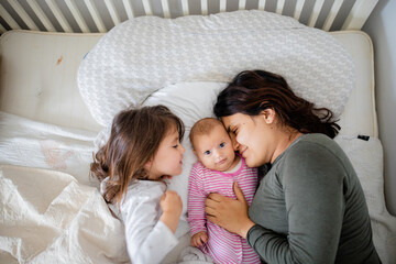 Mother Resting on a Bed with Her Two Happy Young Daughters baby looking directly