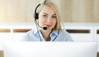 Blonde business woman sitting and communicated by headset in call center in sunny office. Concept...