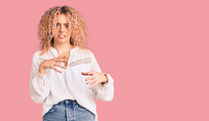 Young blonde woman with curly hair wearing elegant summer shirt disgusted expression, displeased and fearful doing disgust face because aversion reaction. with hands raised