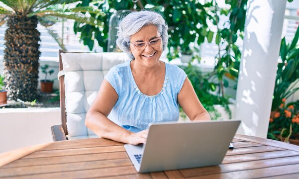 Middle age woman with grey hair smiling happy relaxing sitting at the terrace working from home