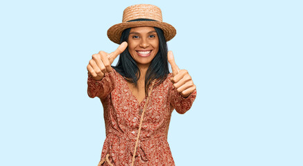 Obraz na płótnie Canvas Young african american woman wearing summer hat approving doing positive gesture with hand, thumbs up smiling and happy for success. winner gesture.