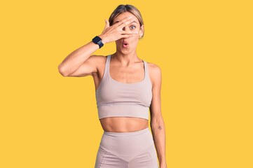 Beautiful caucasian woman wearing sportswear peeking in shock covering face and eyes with hand, looking through fingers with embarrassed expression.