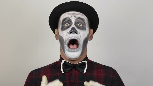 A horrible man in clown makeup sneezes heavily. The scary clown looks at the camera and sneezes violently. Scary grimaces of a clown looking at the camera. Halloween costume.