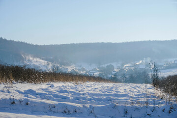 Winter countryside. Snow. Foggy sunny morning. Smoking chimneys in wintertime. Ukraine. Copy space. 