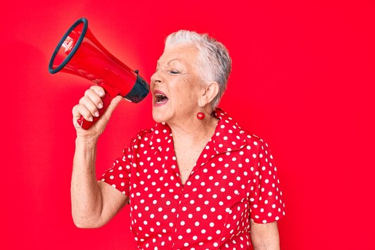 Senior beautiful grey-haired woman screaming using megaphone over isolated red background