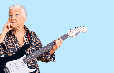 Fototapeta premium Senior beautiful woman with blue eyes and grey hair with modern look playing electric guitar serious face thinking about question with hand on chin, thoughtful about confusing idea