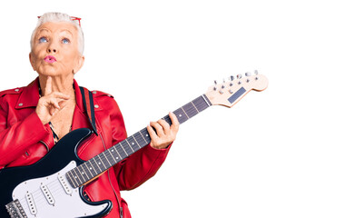 Senior beautiful woman with blue eyes and grey hair wearing a modern look playing electric guitar thinking concentrated about doubt with finger on chin and looking up wondering