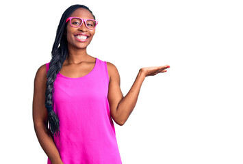 Obraz na płótnie Canvas Young african american woman wearing casual clothes and glasses smiling cheerful presenting and pointing with palm of hand looking at the camera.