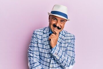 Mature middle east man with mustache wearing vintage and elegant fashion style smiling looking confident at the camera with crossed arms and hand on chin. thinking positive.