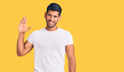 Young latin man wearing casual clothes waiving saying hello happy and smiling, friendly welcome gesture