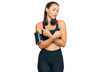 Fototapeta premium Beautiful blonde woman wearing gym clothes and using headphones pointing to both sides with fingers, different direction disagree
