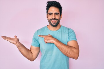Fototapeta premium Handsome hispanic man with beard wearing casual clothes amazed and smiling to the camera while presenting with hand and pointing with finger.