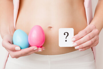 Young woman hands holding two eggs with blue, pink colors and card of question mark. Guessing...