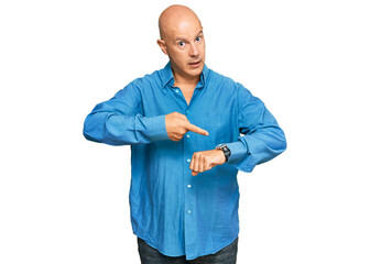 Middle age bald man wearing casual clothes in hurry pointing to watch time, impatience, upset and...