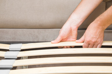 Young man hands putting planks of bed or lamella for mattress. Assembling new textile furniture. Closeup.