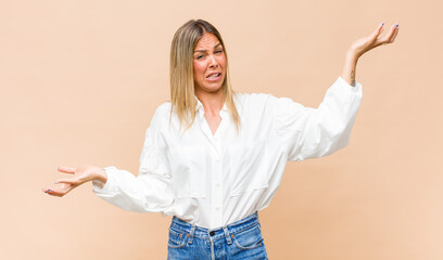 young pretty woman shrugging with a dumb, crazy, confused, puzzled expression, feeling annoyed and...