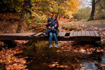 Mother and son in the autumn Park. A woman with a child in her arms, sitting on a wooden bridge.