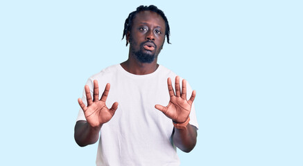 Young african american man with braids wearing casual white tshirt moving away hands palms showing refusal and denial with afraid and disgusting expression. stop and forbidden.