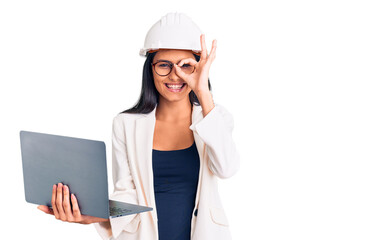 Young beautiful latin girl wearing architect hardhat holding laptop smiling happy doing ok sign with hand on eye looking through fingers
