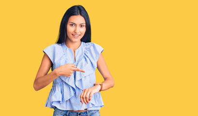 Young beautiful latin girl wearing casual clothes in hurry pointing to watch time, impatience,...