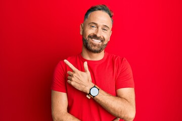 Handsome middle age man wearing casual red tshirt smiling cheerful pointing with hand and finger up to the side