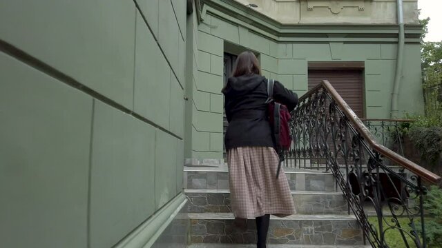 Young business woman goes to her home, gets on the stairs takes keys out of her bag