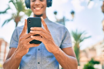 Young african american man smiling happy using smartphone and headphones at the city.