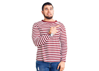 Fototapeta premium Young handsome man wearing striped sweater pointing aside worried and nervous with forefinger, concerned and surprised expression