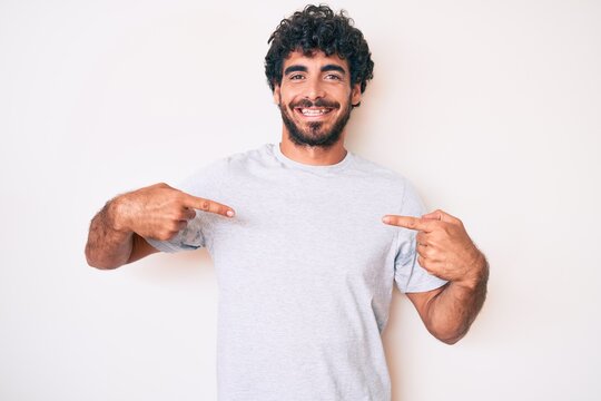Handsome young man with curly hair and bear wearing casual tshirt looking confident with smile on face, pointing oneself with fingers proud and happy.