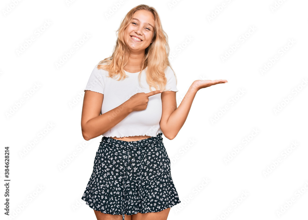 Wall mural young blonde girl wearing casual white tshirt amazed and smiling to the camera while presenting with