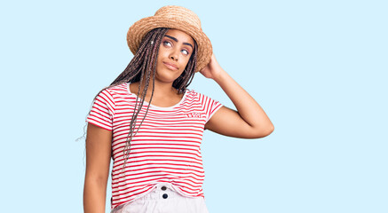 Obraz na płótnie Canvas Young african american woman with braids wearing summer hat confuse and wondering about question. uncertain with doubt, thinking with hand on head. pensive concept.