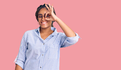 Young african american woman with braids wearing casual clothes and glasses doing ok gesture with hand smiling, eye looking through fingers with happy face.