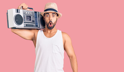 Young hispanic man holding boombox, listening to music scared and amazed with open mouth for surprise, disbelief face